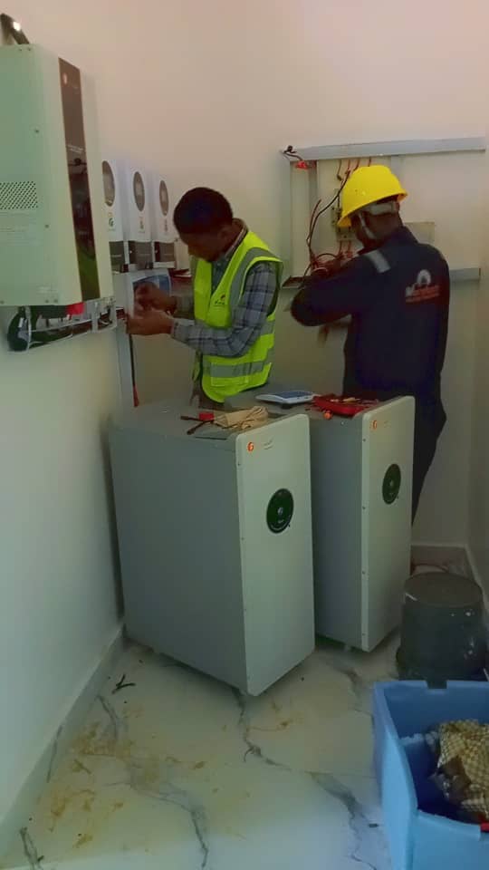 Two technicians working on a battery and inverter installation